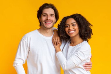 Romantik çok ırklı çift kucaklaşıyor, birlikte poz veriyor ve kameraya gülümsüyor.