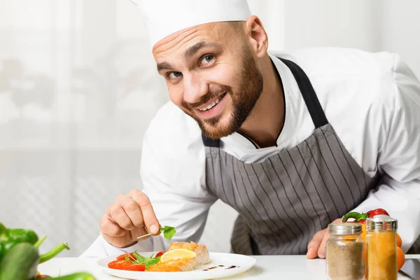 Usmívající se kuchař muž zdobí pečený losos steak v kuchyni — Stock fotografie