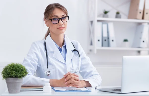 Female Doctor Looking At Camera Sitting At Workdesk In Office — Stok fotoğraf