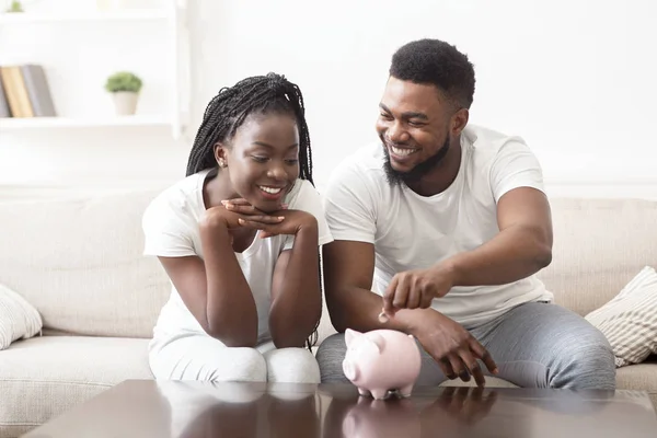 Young Black Couple Putting Coin In Piggybank, Making Savings — Stok Foto