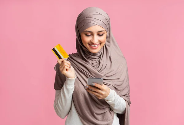 Happy muslim woman in headscarf using smartphone and holding credit card — Stok fotoğraf