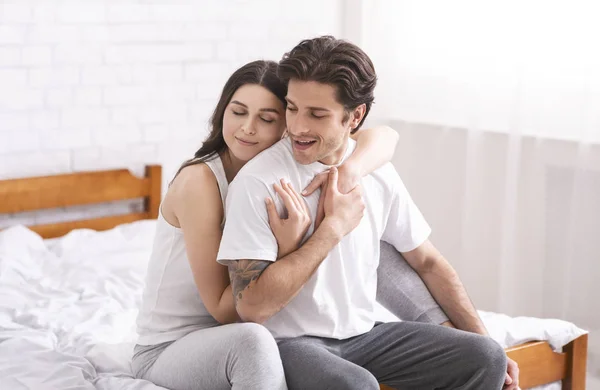 Lykkelige ægtefæller krammer i soveværelset, sidder sammen på sengen - Stock-foto