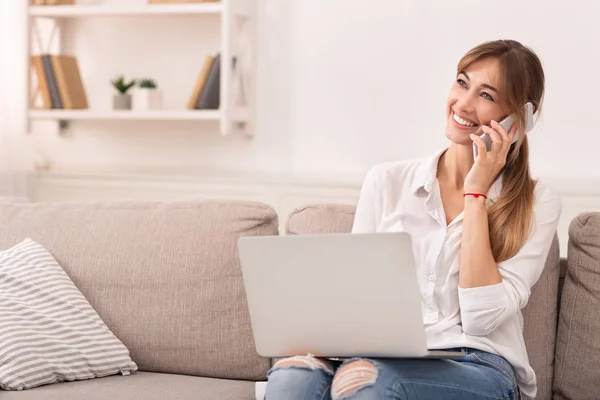 Menina alegre conversando no telefone sentado com laptop interior — Fotografia de Stock