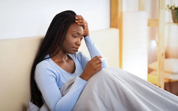 Malade dame noire ayant de la fièvre et des maux de tête assis dans le lit — Photo