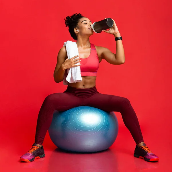 Athletic girl in sportswear on fitness ball drinking sports food