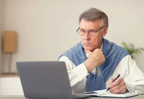 Ανώτερος επιχειρηματίας που εργάζεται στον υπολογιστή κρατώντας σημειώσεις που κάθεται στο γραφείο — Φωτογραφία Αρχείου