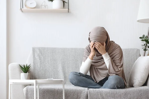 Sconvolto donna musulmana in velo piangendo sul divano a casa — Foto Stock