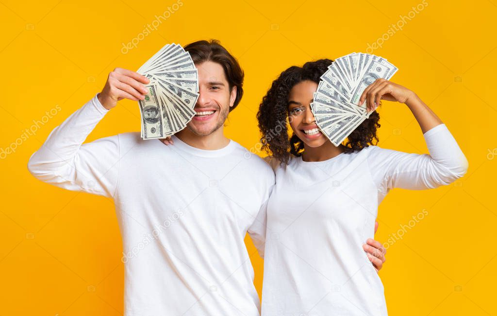 Happy young interracial couple covering eyes with dollar cash