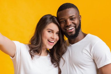 Happy Interracial Couple Taking Selfie, Posing Together Over Yellow Background clipart