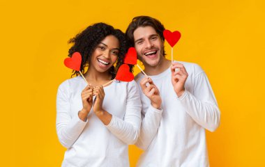 Çubuklarda kırmızı kağıt kalpler tutan romantik çok ırklı çiftin portresi.