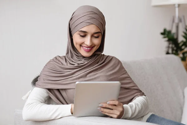 Senyum muslim wanita dalam jilbab menggunakan tablet digital, santai di rumah — Stok Foto