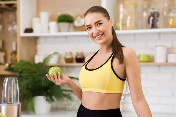 Fitte Frau isst Apfel zum Frühstück, steht in der Küche — Stockfoto