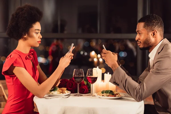 Афро-американская пара с помощью мобильных телефонов, имеющих свидание в ресторане — стоковое фото