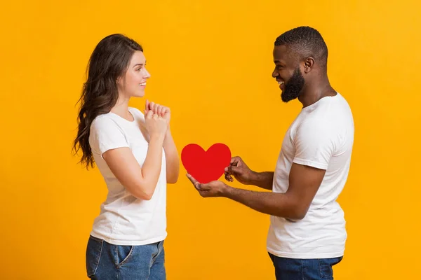 Romántico negro novio presentando rojo papel corazón a su sorprendido novia — Foto de Stock