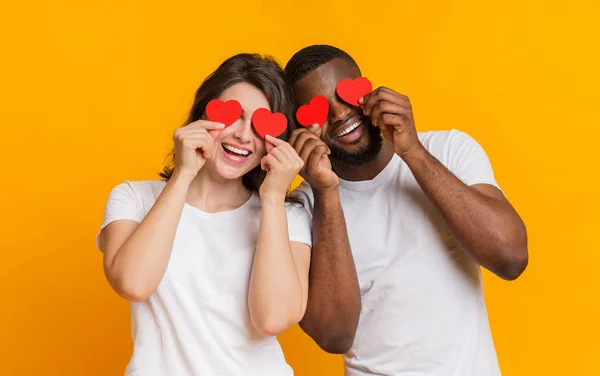 Romantisches multiethnisches Paar posiert mit roten Herzen über den Augen und lacht — Stockfoto