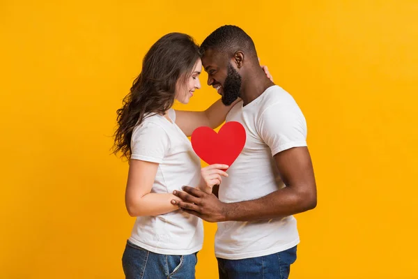 Romántica pareja interracial sosteniendo el corazón de papel rojo y tocando los frentes — Foto de Stock