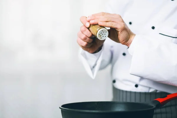 Chef aggiungendo pepe in padella in piedi in cucina al coperto, Ritagliato — Foto Stock