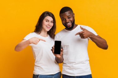 Siyah ekranlı akıllı telefonu tutan ve işaret eden mutlu çok ırklı çift.
