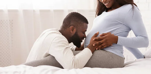 Preto homem abraçando seu grávida mulher barriga e beijá-lo — Fotografia de Stock