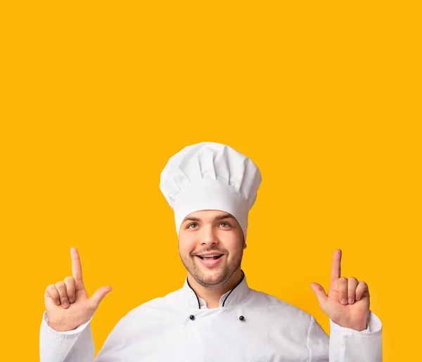 Sorrindo Chef Man apontando os dedos para cima sobre fundo de estúdio amarelo — Fotografia de Stock