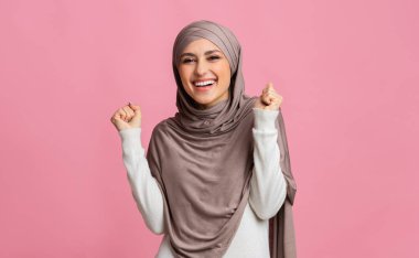 Heyecanlı Orta Doğulu kadın başarıyı kutluyor, ellerini kaldırıyor ve yumruklarını sıkıyor.