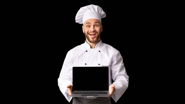 Küchenchef hält Laptop mit leerem Bildschirm im Stehen, schwarzer Hintergrund — Stockfoto