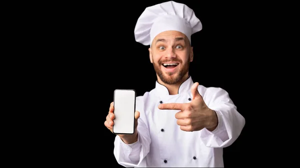 Cocinero hombre mostrando teléfono pantalla vacía de pie sobre fondo negro — Foto de Stock