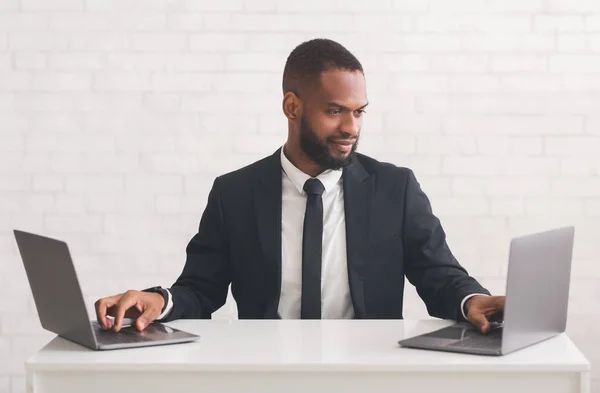 Afro hombre de negocios escribiendo en dos computadoras portátiles sobre fondo blanco —  Fotos de Stock