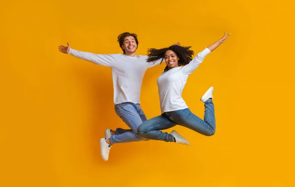 Obekymmersfri interracial par hoppar i luften med spridda armar — Stockfoto