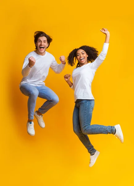 Joyful multiracial couple jumping, having fun together on yellow background — 스톡 사진