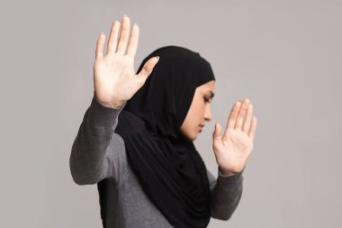 Korkmuş Arap kız dur işareti yapıyor, kendini şiddetten koruyor.