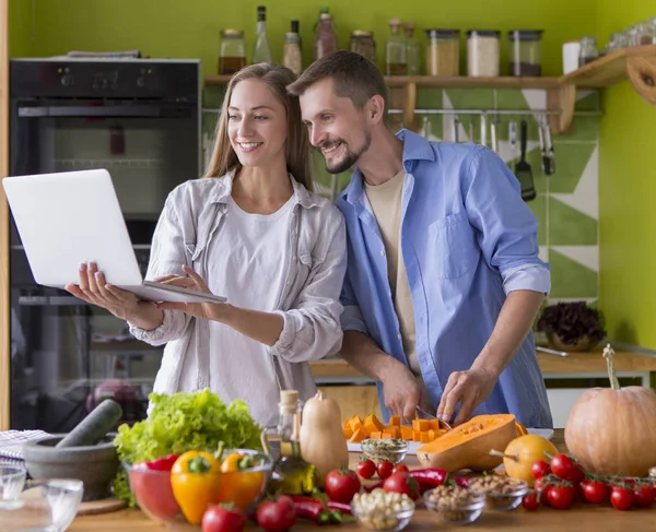 Härligt par i köket letar recept på laptop och matlagning — Stockfoto