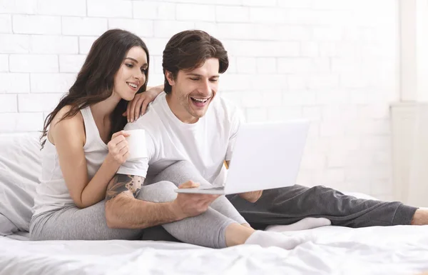 Возбужденные супруги наслаждаются информацией на ноутбуке, отдыхают в постели — стоковое фото