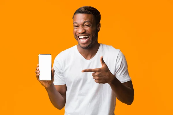 Guy apontando o dedo na tela do telefone rindo, fundo laranja, Mockup — Fotografia de Stock