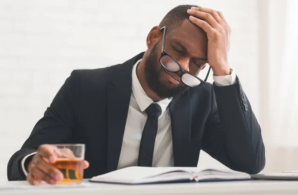 Hombre afro agotado en traje bebiendo alcohol, tocándose la cabeza —  Fotos de Stock