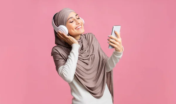 Happy muslim girl in wireless headphone listening music online on smartphone — Stok Foto