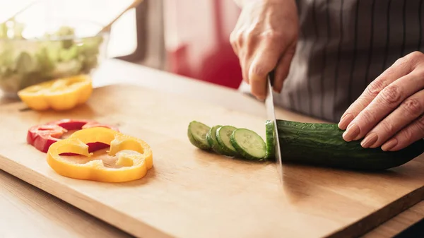 Senior woman cutting fresh pepper and cucumber at kitchen — 스톡 사진