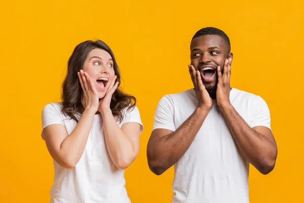 Förvånad ung kvinna och svart man röra deras kinder med förvåning — Stockfoto
