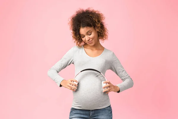 Terhesség és zene. Afro várandós nő kezében fülhallgató közelében has — Stock Fotó