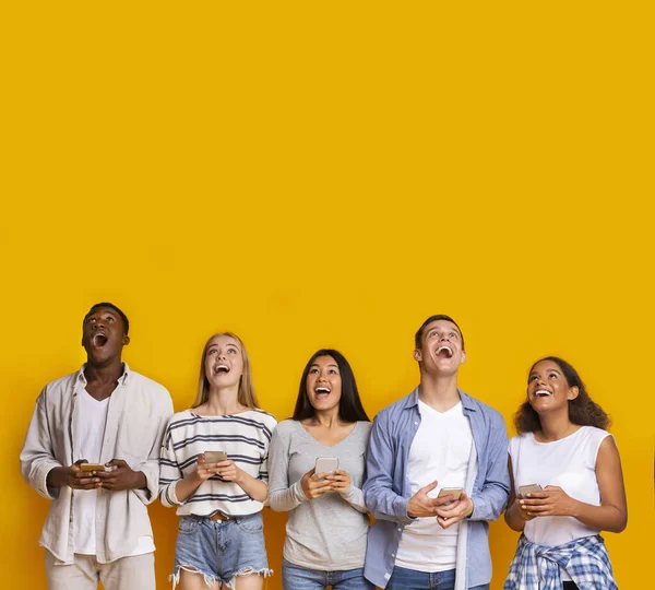 Grupo de estudiantes sorprendidos con teléfonos inteligentes sobre fondo amarillo —  Fotos de Stock