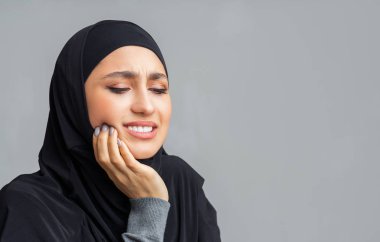 Diş ağrısı çeken Arap kız, iltihaplı yanağına dokunuyor.