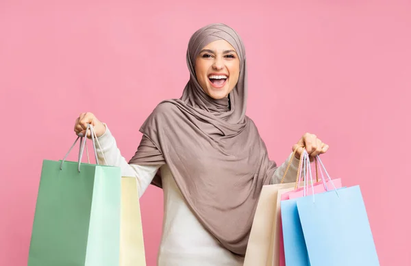 Mujer islámica alegre en pañuelo para la cabeza sosteniendo gran cantidad de bolsas de comprador brillantes —  Fotos de Stock