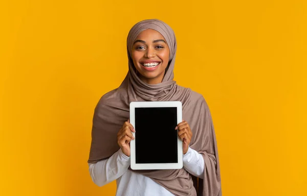 Mujer afro sonriente en pañuelo para la cabeza demostrando tableta digital con pantalla negra —  Fotos de Stock