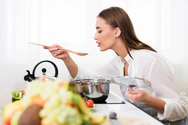 Jahrtausendfrau kocht und probiert Suppe mit Löffel — Stockfoto