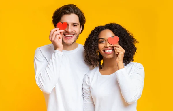 Retrato de feliz pareja interracial con corazones de papel rojo sobre los ojos — Foto de Stock