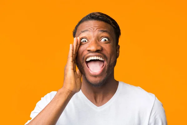 Zabawny Afro facet krzyczy trzymając się za rękę w pobliżu ust w studio — Zdjęcie stockowe