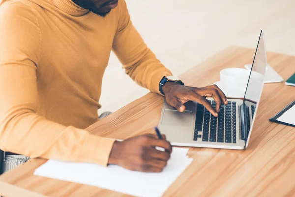 Felismerhetetlen afro srác dolgozik a laptopján és az írás — Stock Fotó