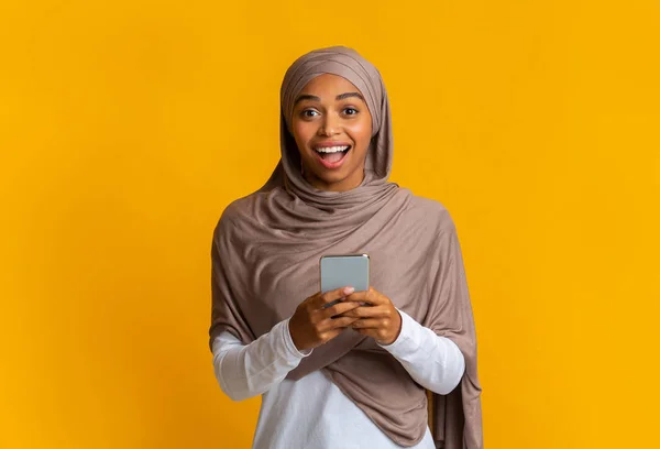 Gembira afro muslim gadis memegang smartphone di tangan dan melihat kamera — Stok Foto