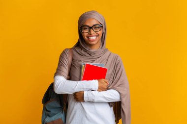 Sırt çantası ve not defterleriyle tesettürlü mutlu siyah Müslüman öğrenci kız.