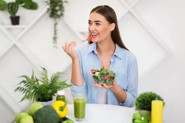 Mulher sorridente comendo salada mista fresca na cozinha moderna — Fotografia de Stock